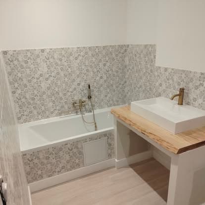 Salle de bain finie : baignoire îlot, faïence motif géométrique gris blanc, plan vasque bois massif et robinetterie or brossé