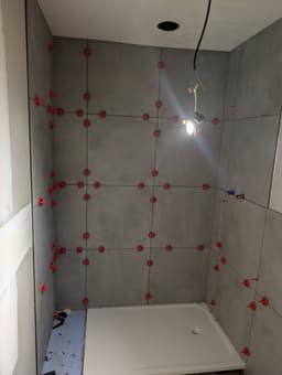 Douche en cours de pose avec receveur extra-plat et carrelage mural gris grand format en cours de calage