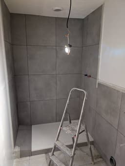 Douche presque terminée avec receveur blanc et carrelage gris grand format posé sur les parois et le sol