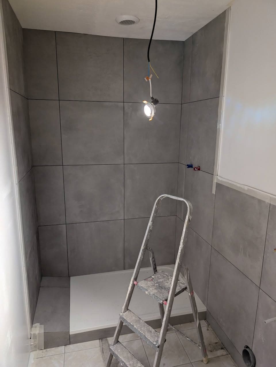 Douche presque terminée avec receveur blanc et carrelage gris grand format posé sur les parois et le sol