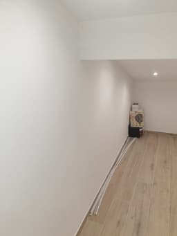 Couloir rénové avec murs blancs, sol clair et plinthes en cours de finition