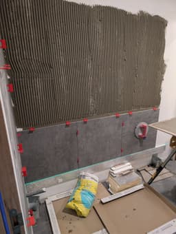 Pose de carrelage mural gris avec colle peignée et croisillons sur support préparé