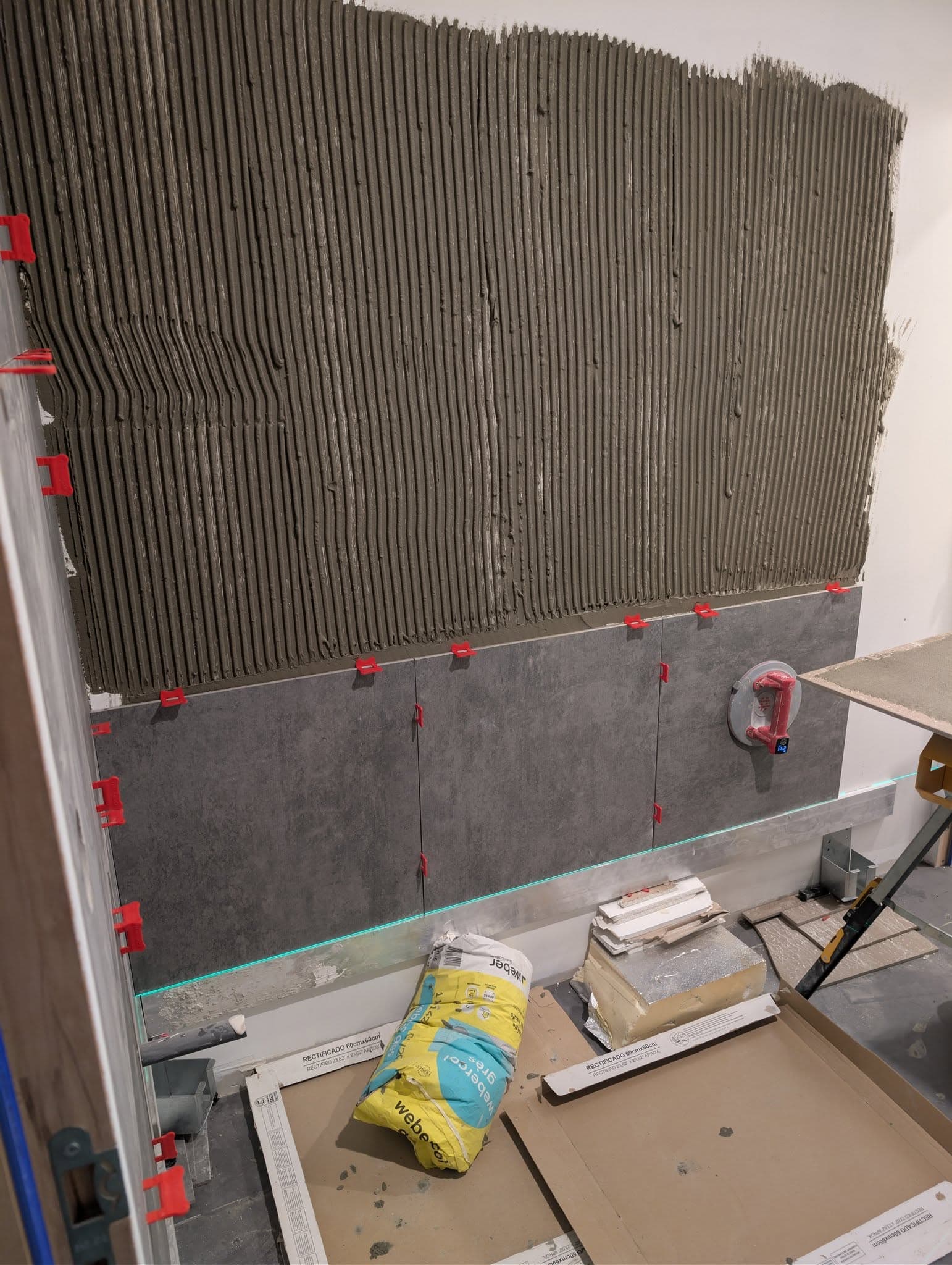 Pose de carrelage mural gris avec colle peignée et croisillons sur support préparé