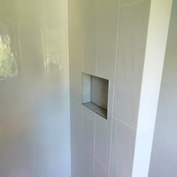 Détail douche : faïence blanche pose verticale, niche encastrée avec carrelage effet pierre gris et profil chrome