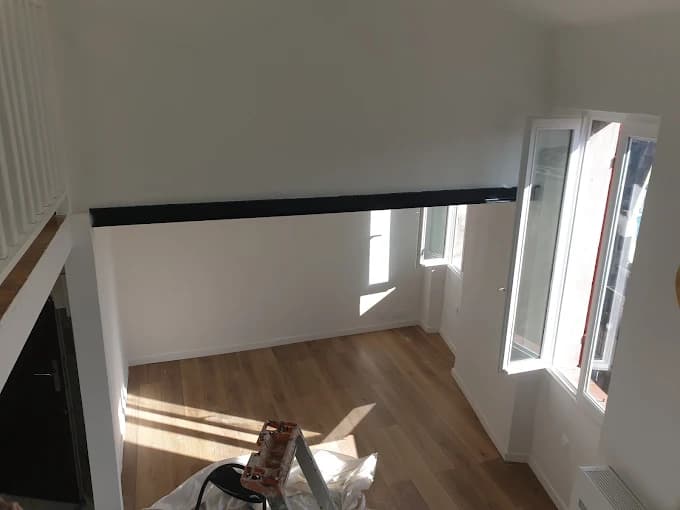 Pièce blanche sous mezzanine : IPN noir, parquet clair, grandes fenêtres