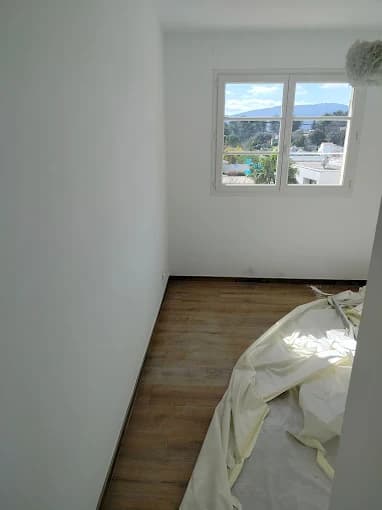 Chambre : murs blancs, parquet clair, fenêtre avec vue