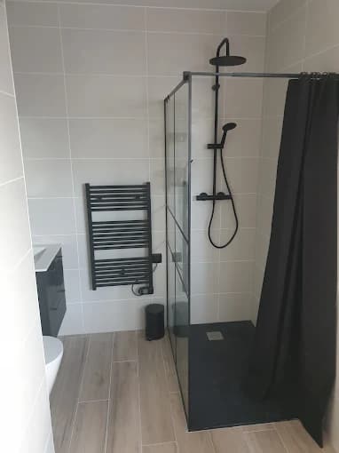 Salle de bain : douche noir mat, faïence beige, sol aspect bois