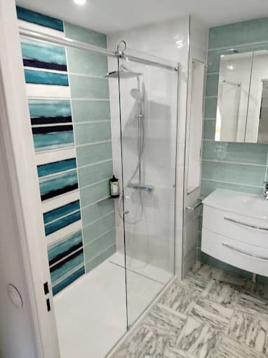 Salle de bain finie : faïence bleu-vert, douche vitrée, meuble suspendu