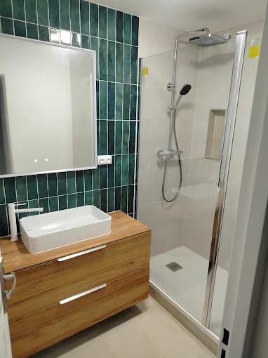 Salle de bain : faïence verte, douche vitrée, meuble vasque bois et vasque à poser