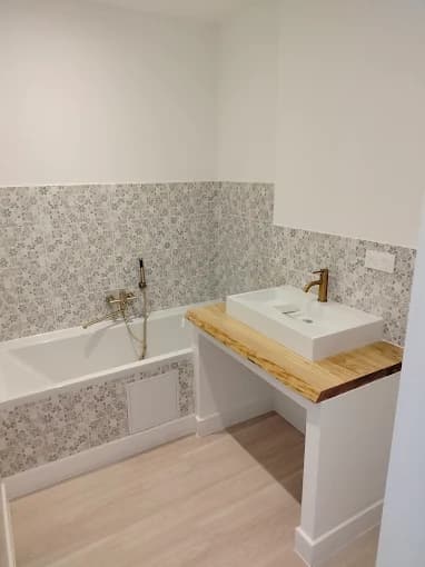 Salle de bain : motif gris au sol et sur le mur, bois brut et détails métal brossé (cadrage sans appareils sanitaires)