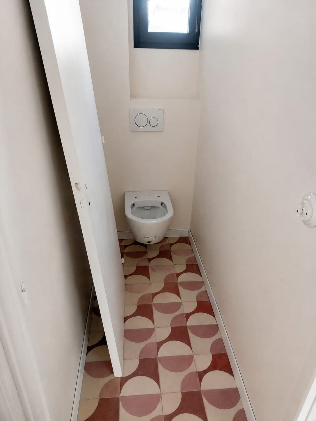 Petit WC avec sol à motifs géométriques rouge et blanc.