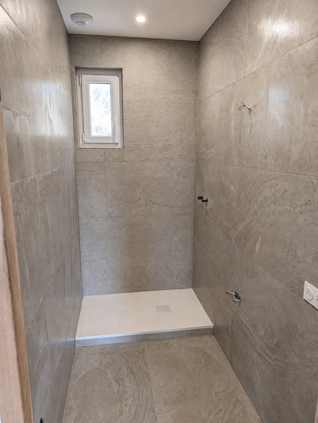 Douche à l'italienne avec grand carrelage gris sur murs et sol.