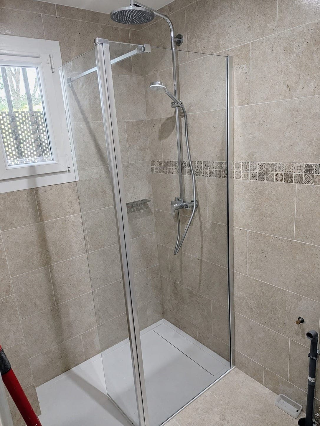 Douche vitrée avec carrelage beige et frise décorative.