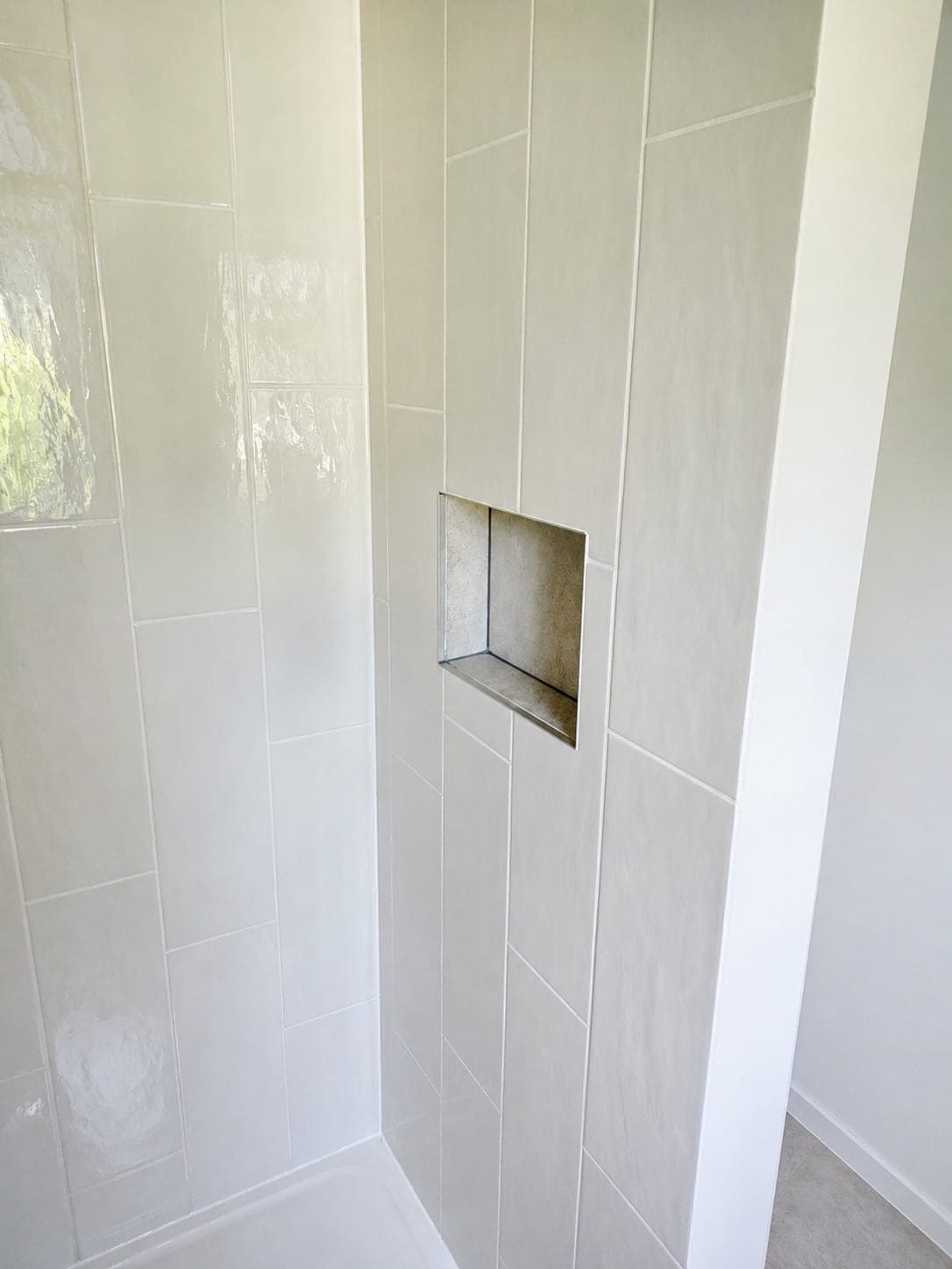 Paroi de douche en carrelage blanc brillant avec niche intégrée.
