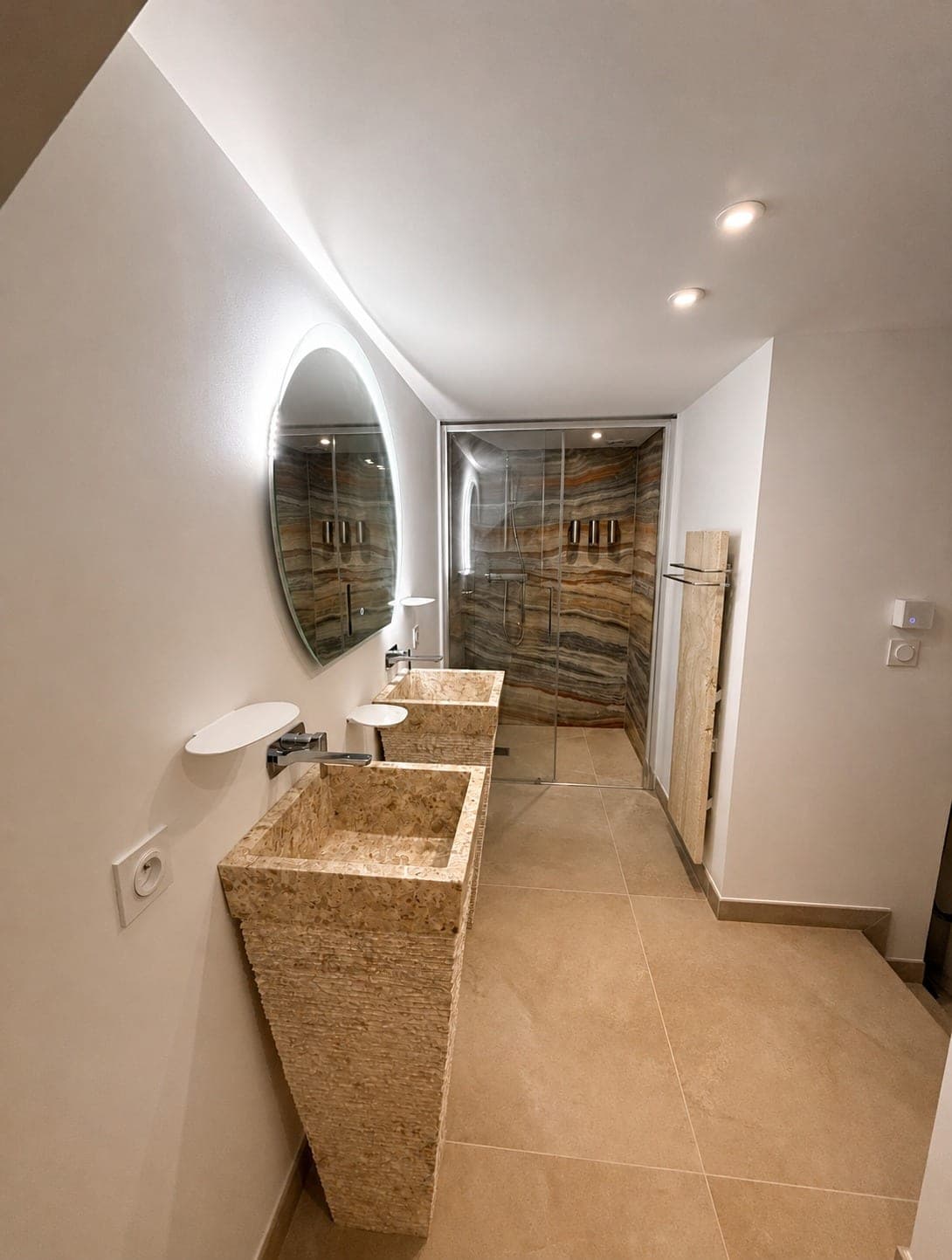 Salle de bain avec sols et murs carrelés autour de vasques en pierre.