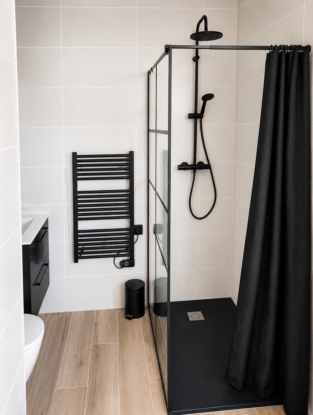 Douche noire et blanche avec sol effet bois et parois carrelées.