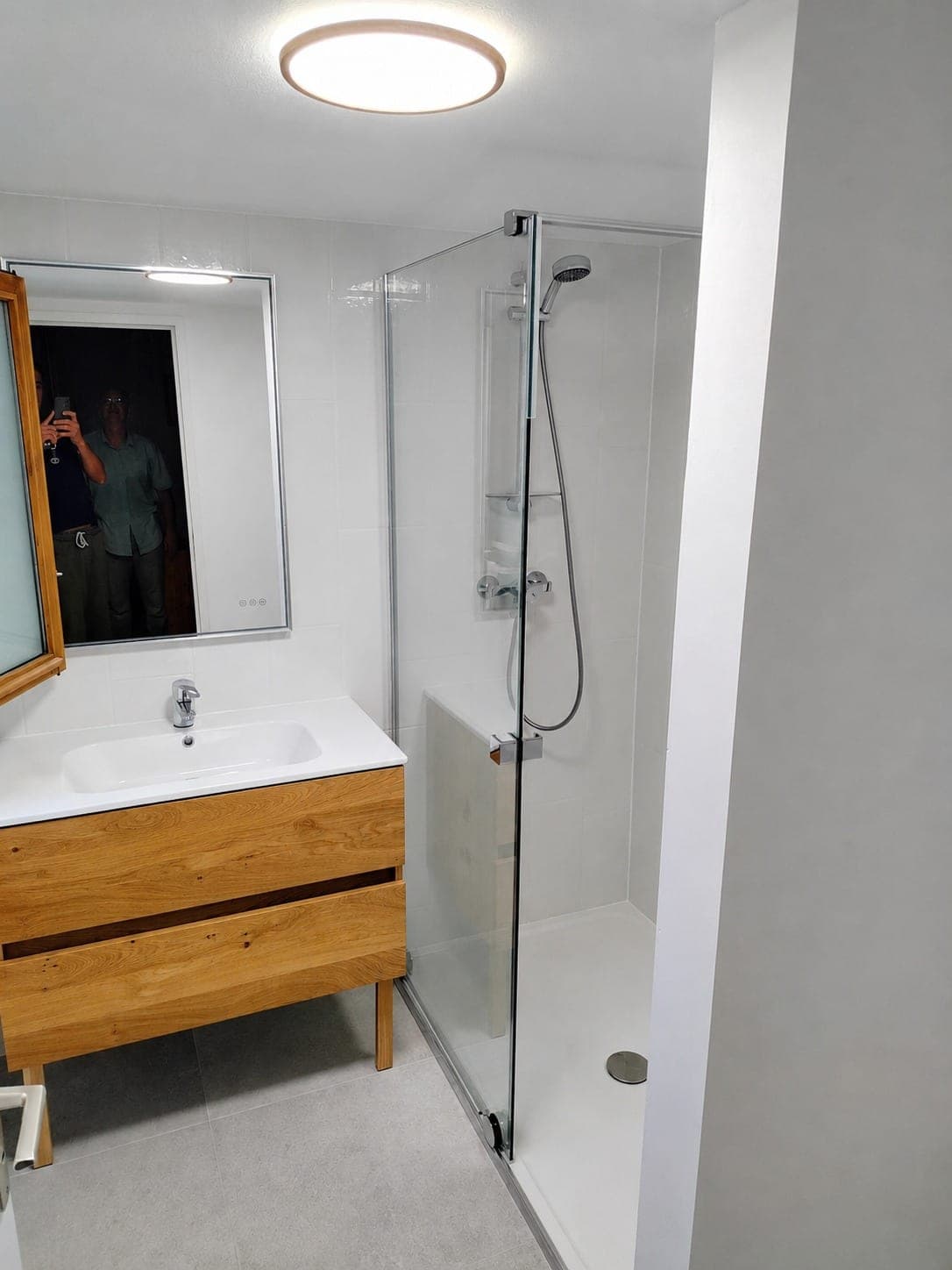 Salle de bain blanche avec douche vitrée et meuble bois.