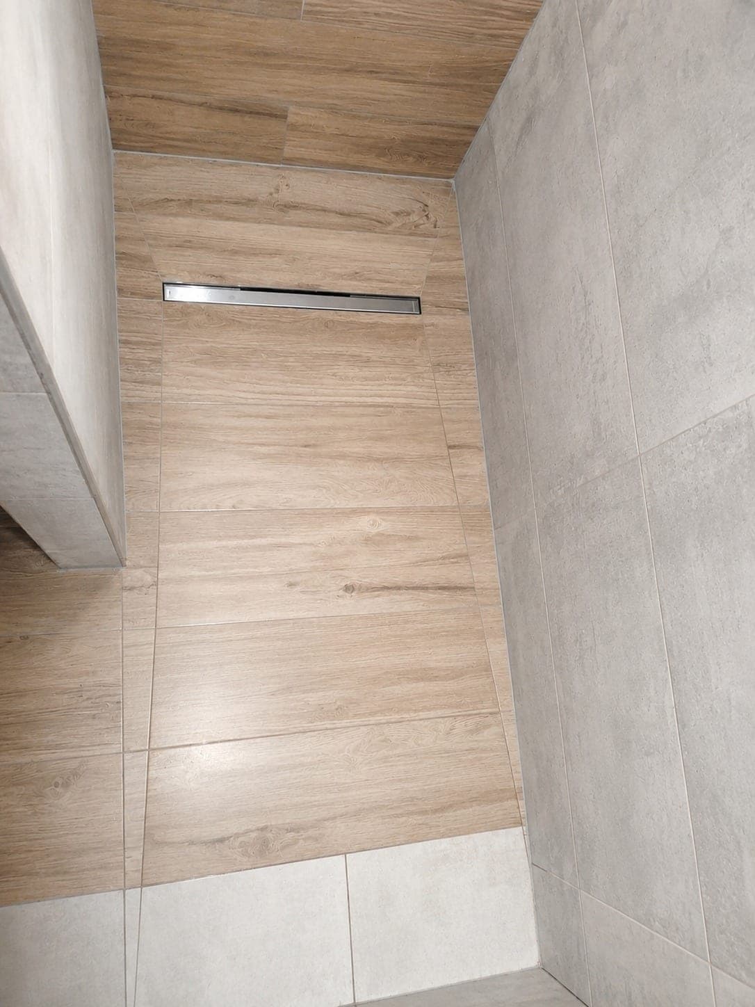 Vue plongeante d'une douche avec sol effet bois et mur gris.