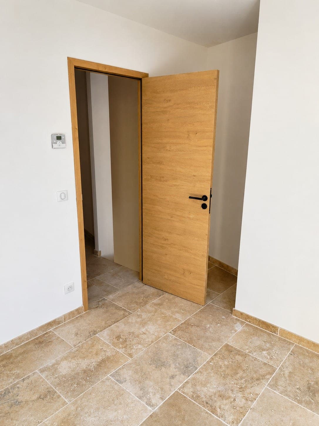 Mur blanc fini autour d'une porte bois dans une pièce carrelée.