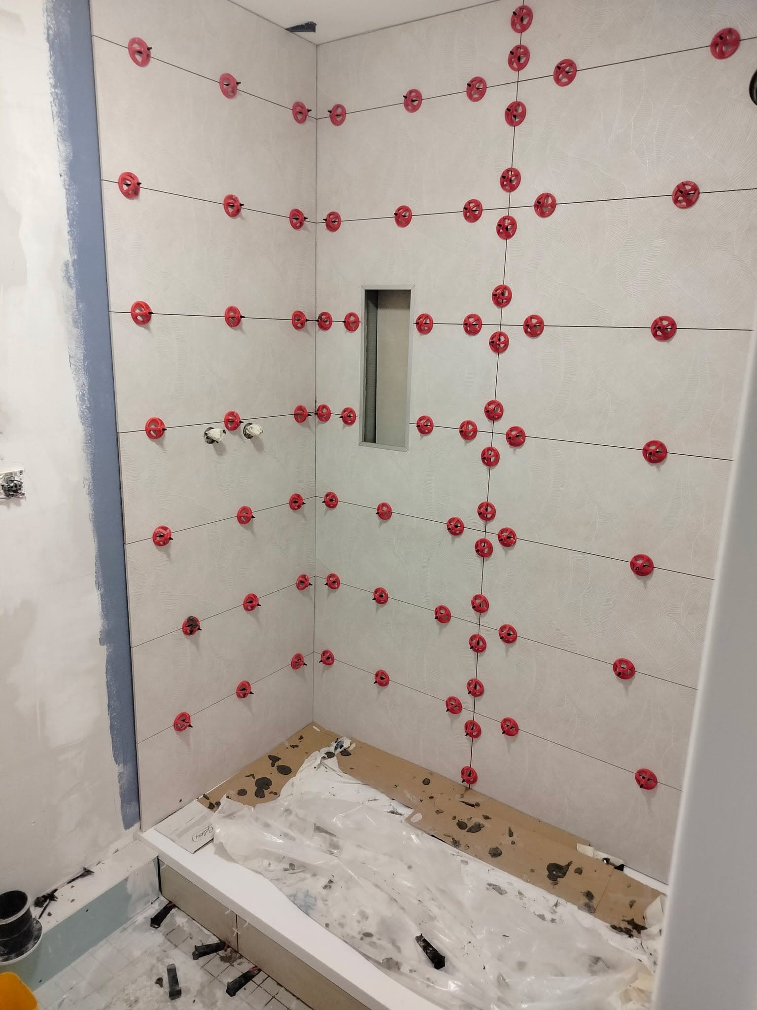 Préparation d'une douche avec carrelage mural vert, croisillons et niche intégrée